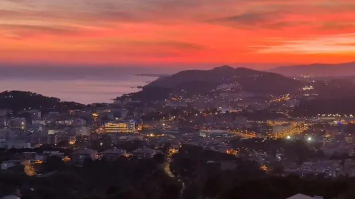Vue panoramique sur une ville côtière illuminée au coucher du soleil.