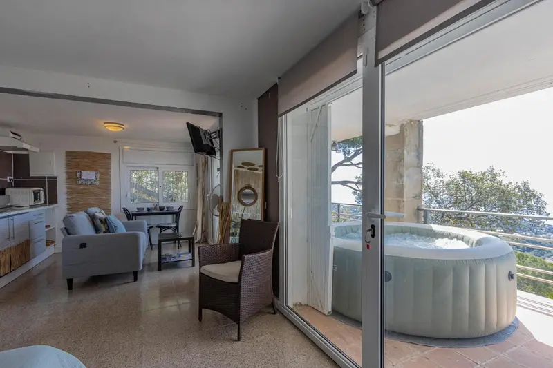 Espace de vie lumineux avec canapé, cuisine et accès à une terrasse avec jacuzzi.