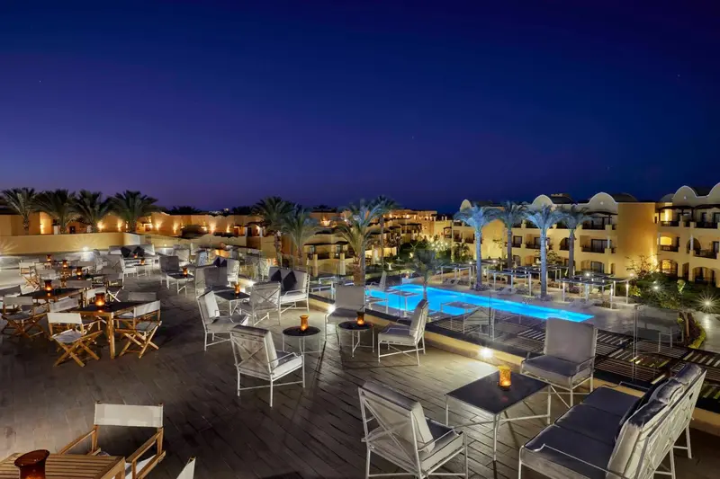 Terrasse lumineuse avec tables et chaises près d'une piscine éclairée.