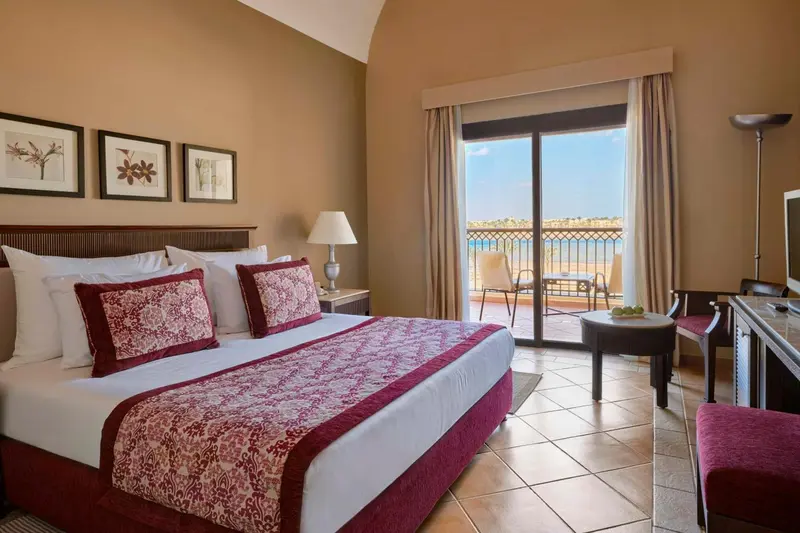 Chambre lumineuse avec un grand lit et une vue sur la mer depuis un balcon.