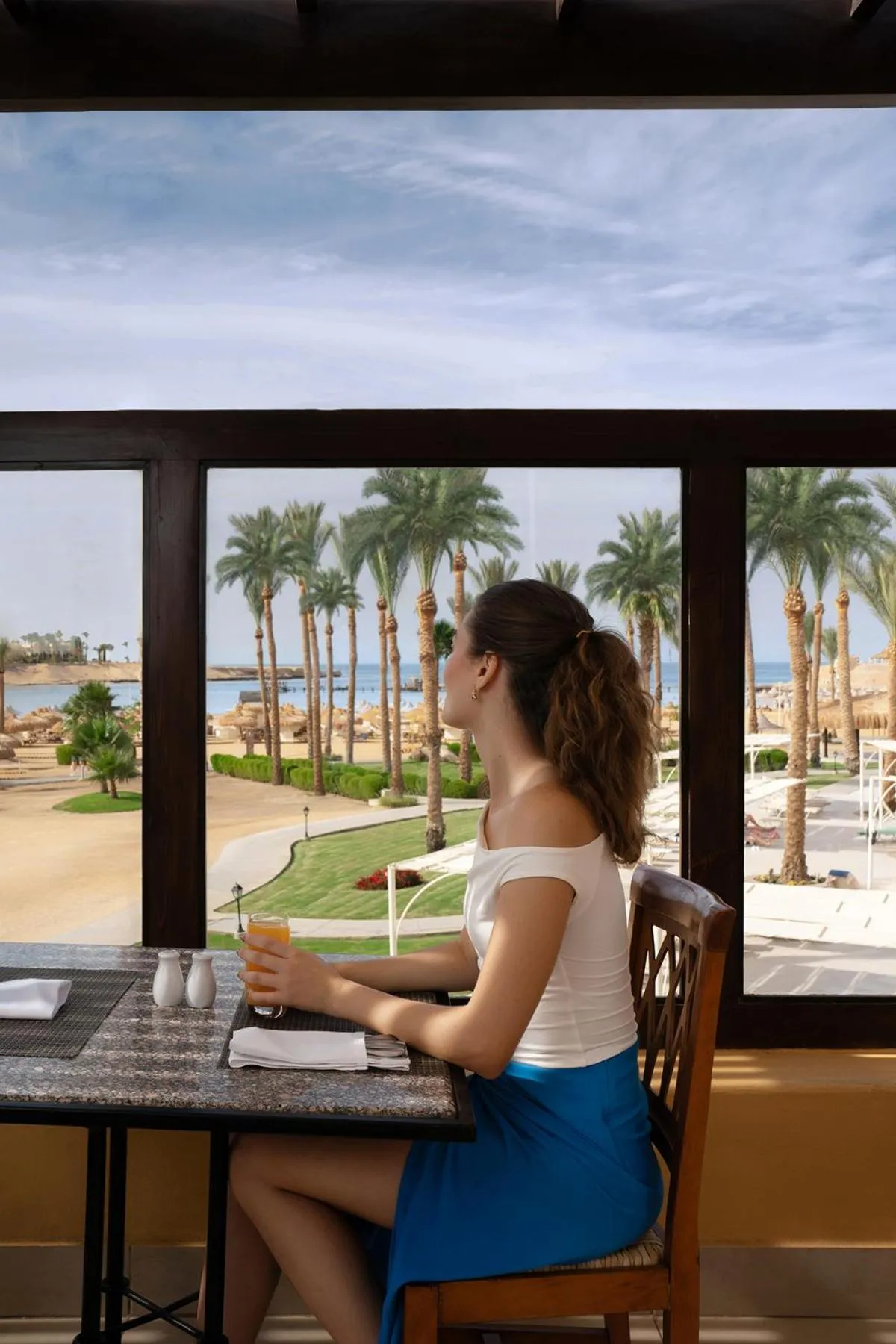 Une femme assise à une table de restaurant avec vue sur la mer et les palmiers.