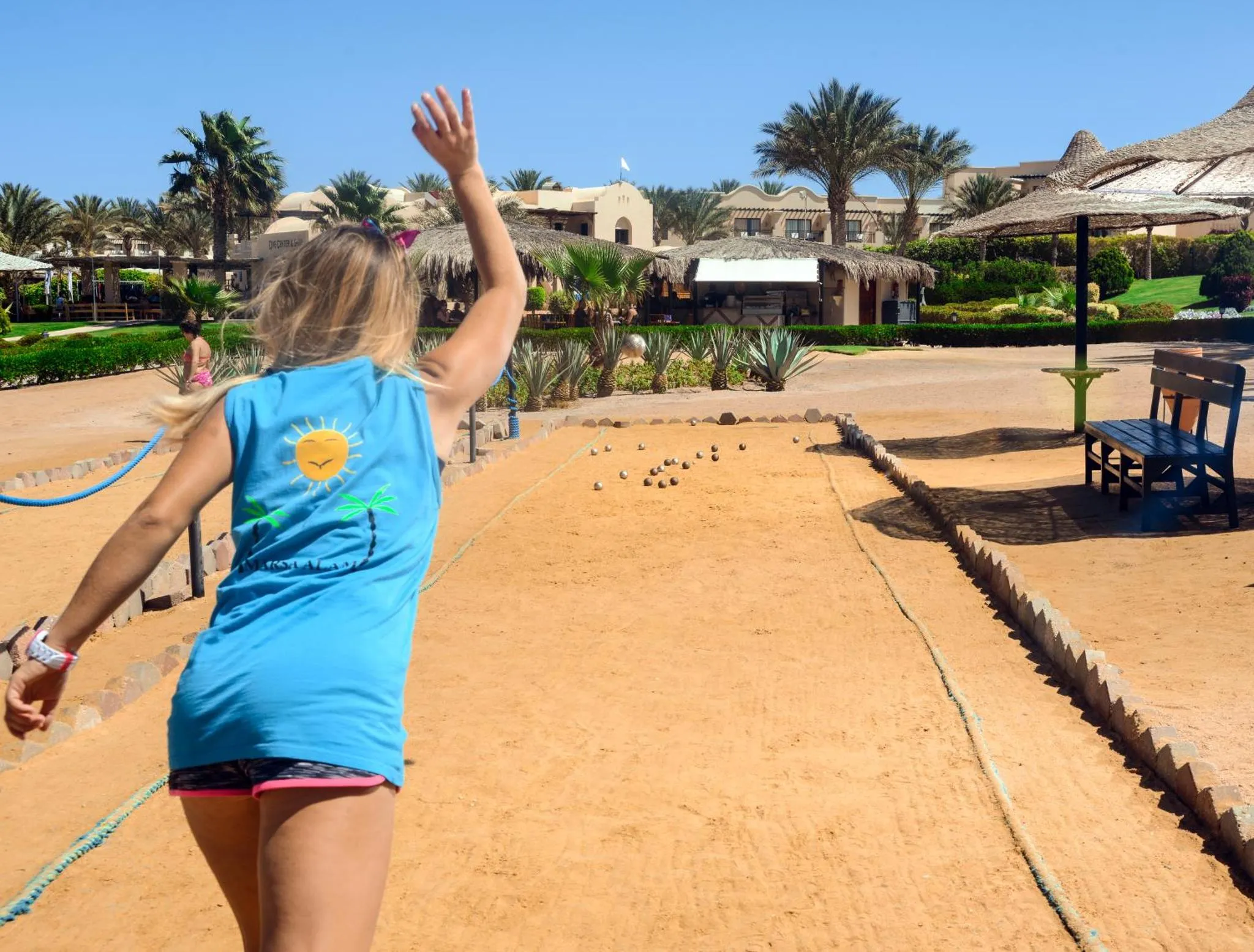 Une personne lance une boule sur une aire de jeu de pétanque en bord de mer.