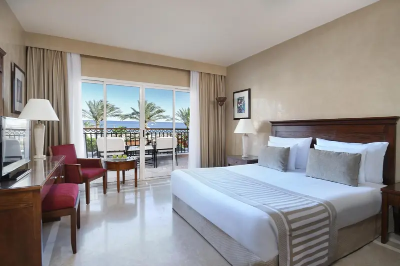 Chambre lumineuse avec un grand lit et un accès à un balcon offrant une vue sur la mer.