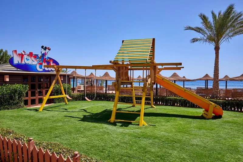 Structure de jeux en bois sur une pelouse verdoyante, avec la mer en arrière-plan.