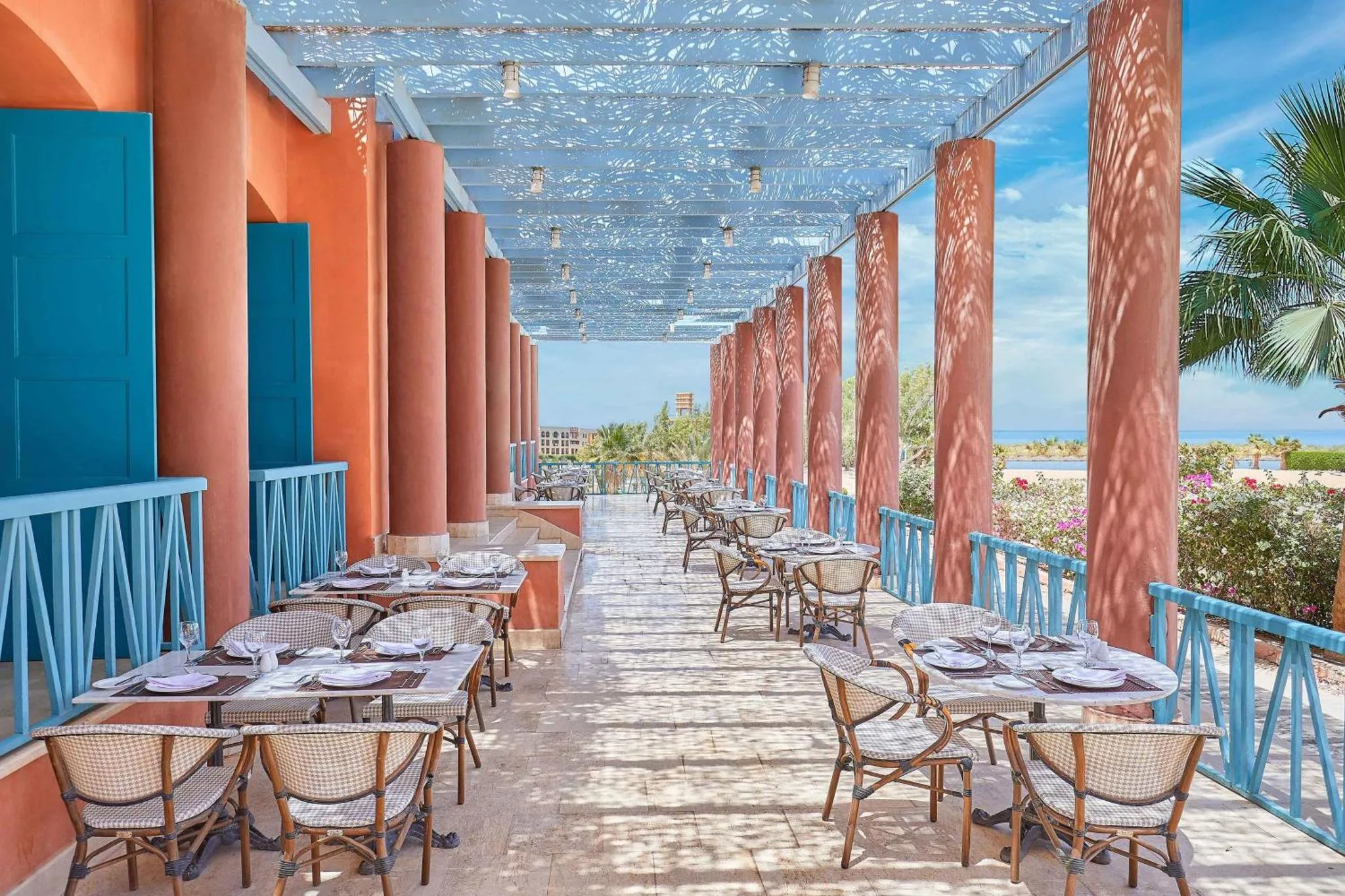 Terrasse ombragée avec tables et chaises donnant sur la mer.