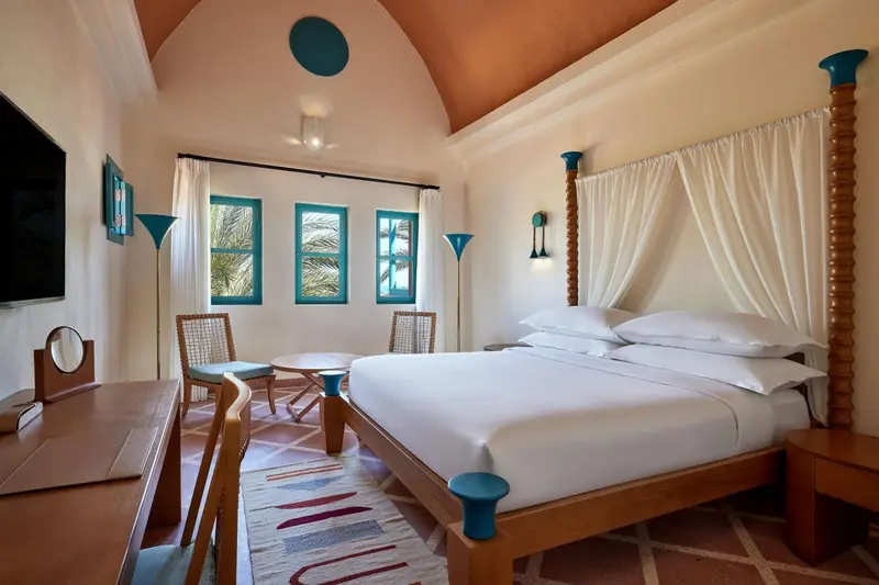 Une chambre lumineuse avec un lit recouvert de blanc et deux fauteuils.