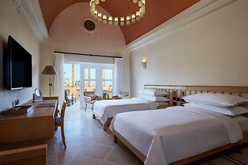Une chambre lumineuse avec deux lits simples et une porte-fenêtre donnant sur une terrasse.