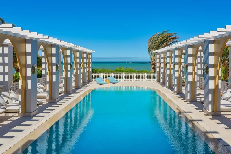 Une piscine rectangulaire bordée d'une pergola blanche et de transats.