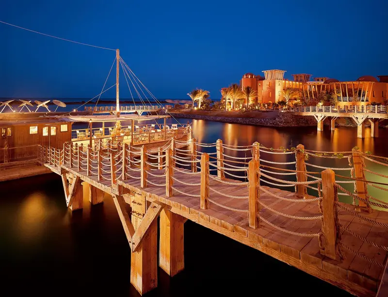 Ponton en bois illuminé menant à un bâtiment au bord de l'eau au crépuscule.