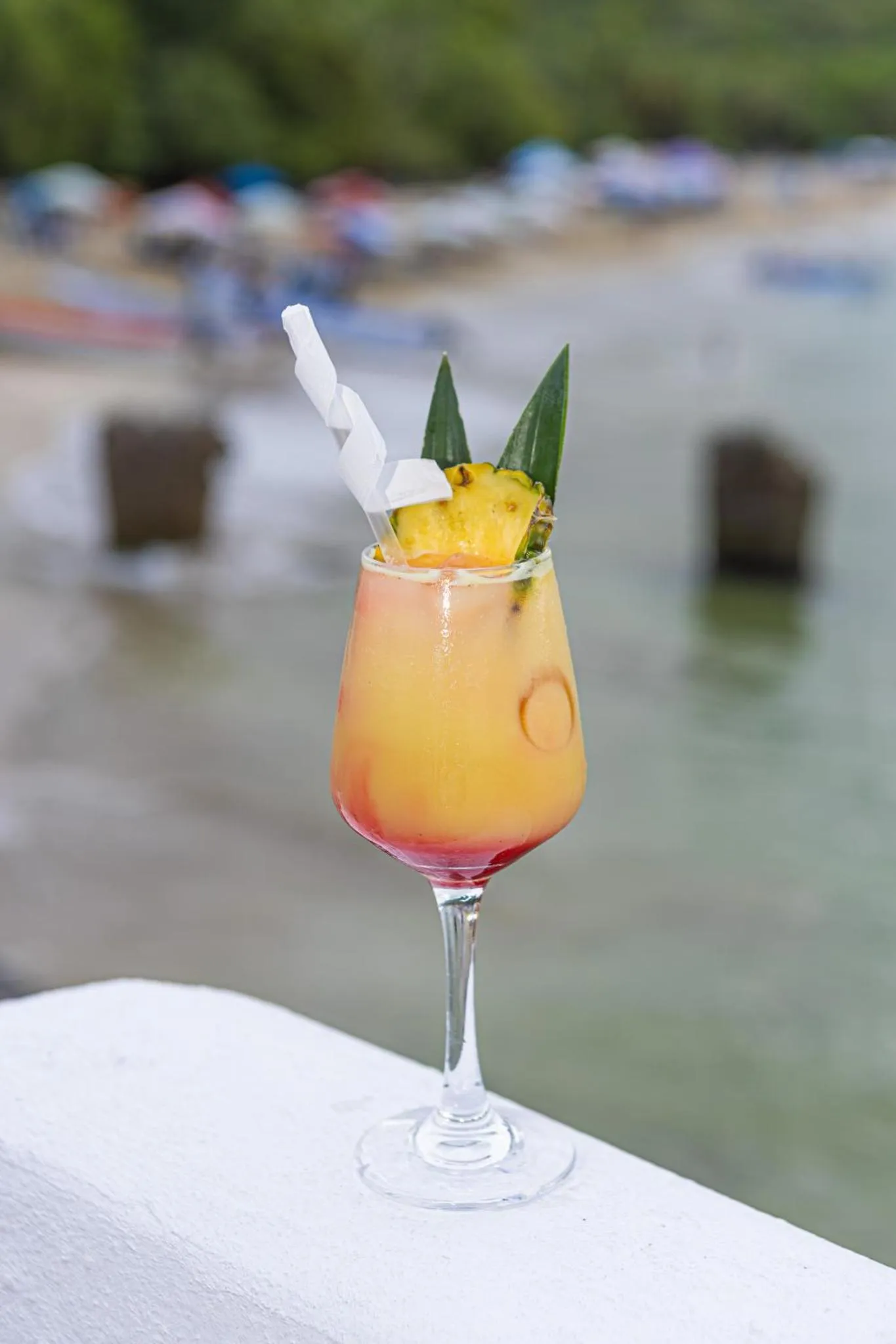 Un cocktail coloré à l'ananas est présenté sur une table blanche en bord de mer.