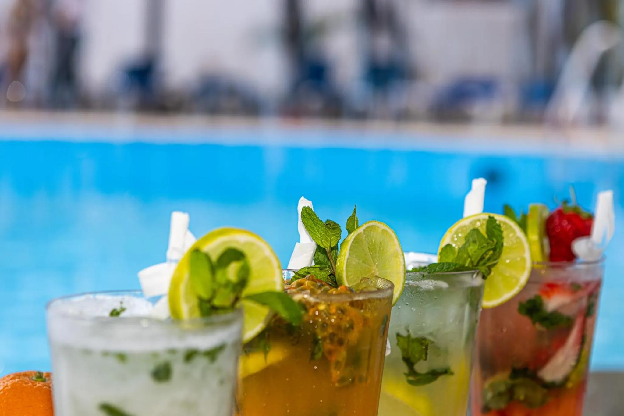 Des cocktails colorés sont présentés au bord d'une piscine ensoleillée.