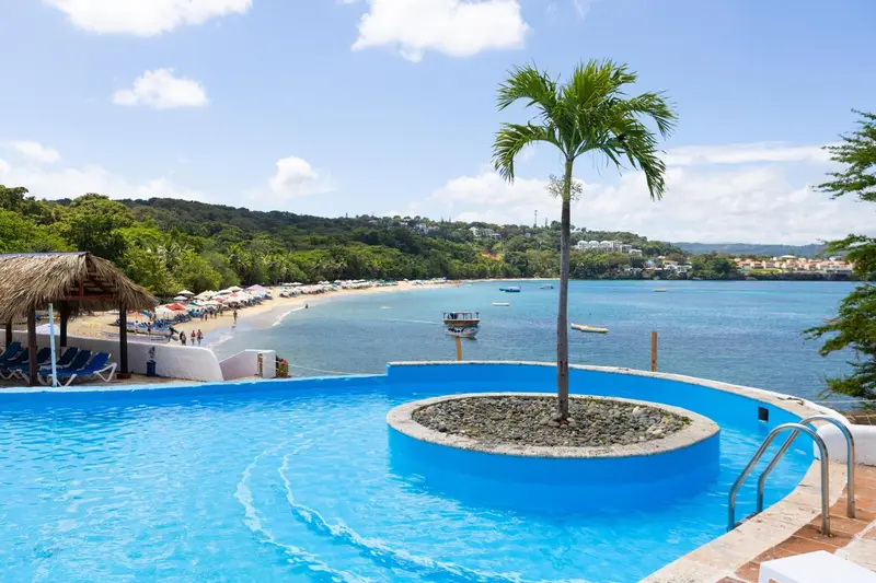 Vue sur une piscine à débordement donnant sur une plage et la mer.