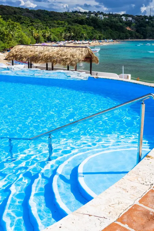 Une piscine turquoise avec des marches et une vue sur une plage.