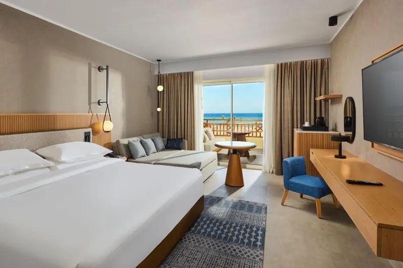 Une chambre lumineuse avec un grand lit et un accès à un balcon avec vue sur la mer.