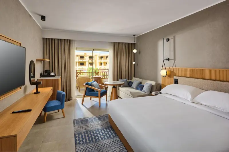 Chambre lumineuse avec un lit confortable et un coin salon donnant sur une terrasse.
