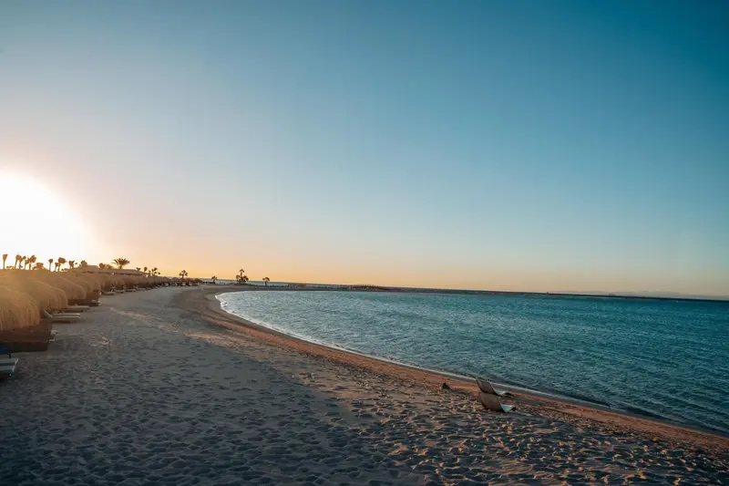 Plage de sable fin bordée d'une mer turquoise sous un ciel clair.