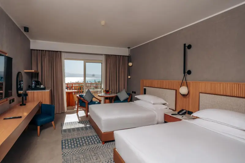 Une chambre lumineuse avec deux lits et un coin repas près d'une baie vitrée.