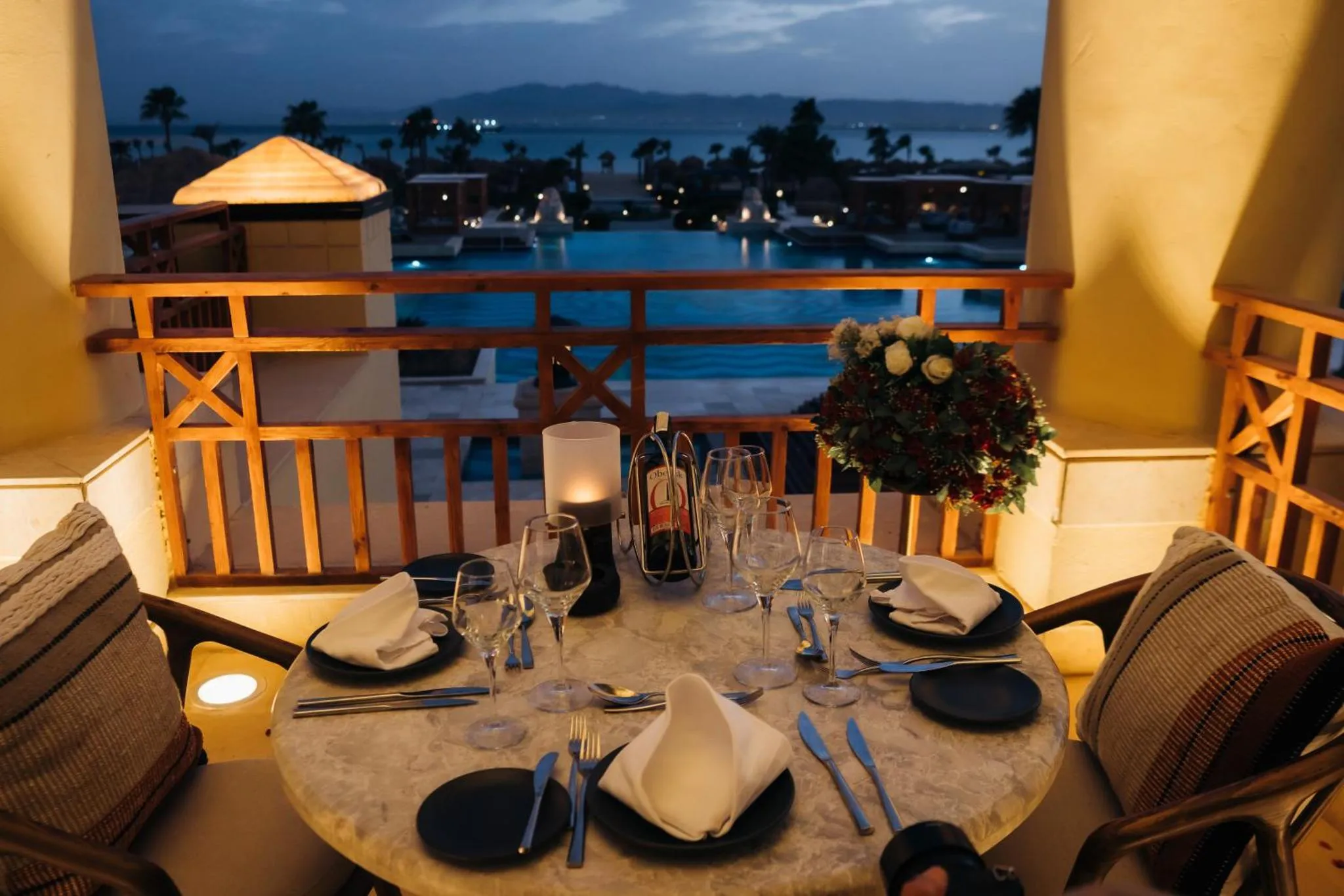 Table dressée sur une terrasse avec vue sur la mer et une piscine illuminée.