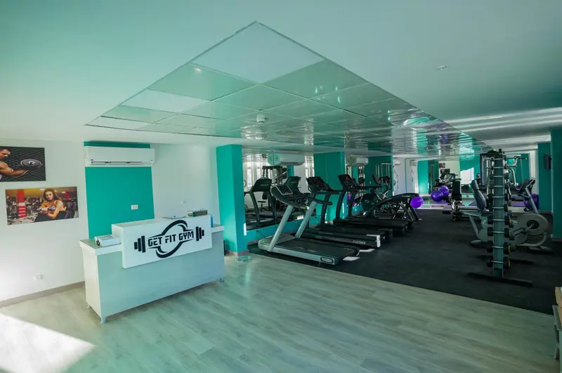 Une salle de sport lumineuse avec des équipements de fitness et un comptoir d'accueil.