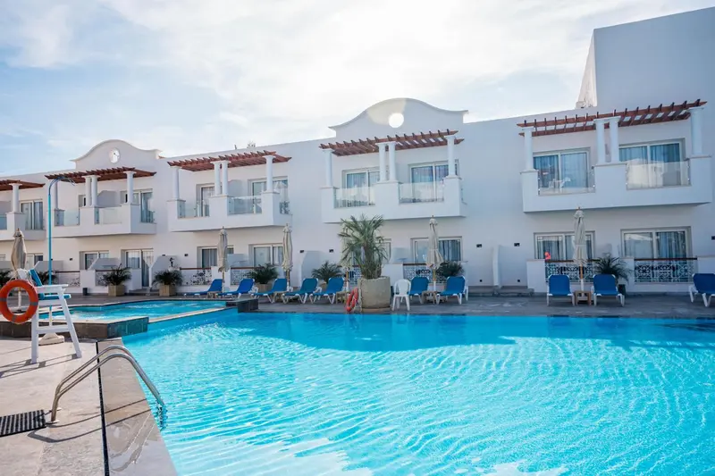 Piscine turquoise bordée de transats bleus devant un bâtiment blanc à balcons.