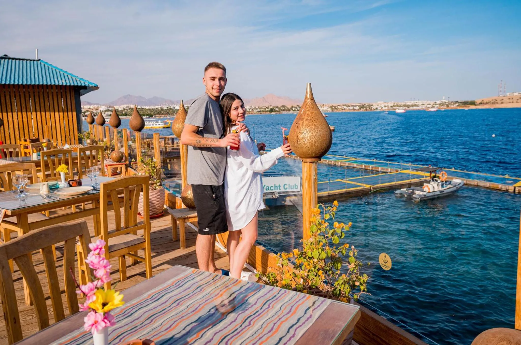 Un couple se tient sur une terrasse en bois avec vue sur la mer.