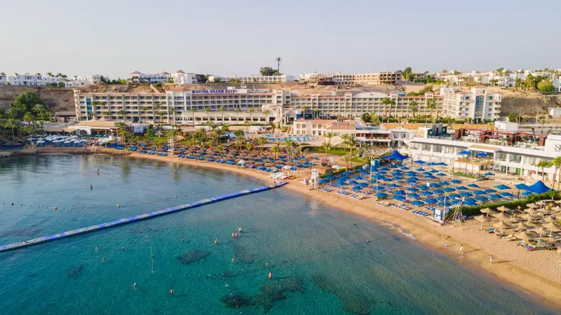 Vue aérienne d'une plage ensoleillée bordée de transats et d'un hôtel.