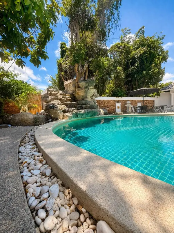 Une piscine turquoise bordée de galets blancs et de végétation luxuriante.