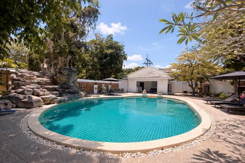 Piscine extérieure entourée d'une végétation luxuriante et de chaises longues.