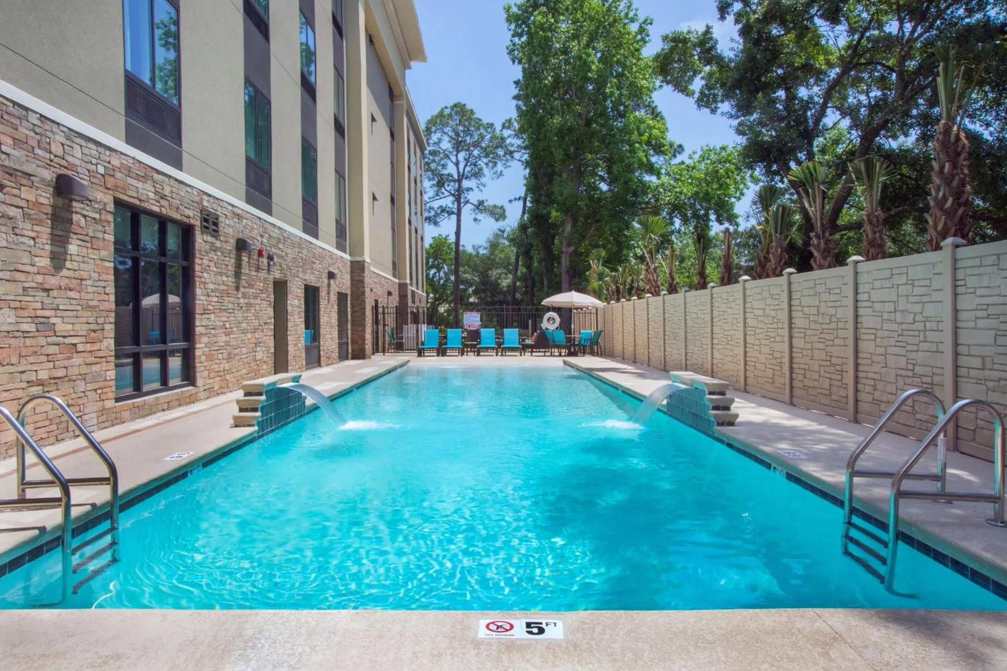Une piscine rectangulaire avec une cascade et des transats bleus au bord.