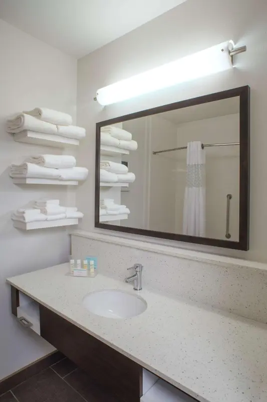 Une salle de bain lumineuse avec un grand miroir et des serviettes pliées.