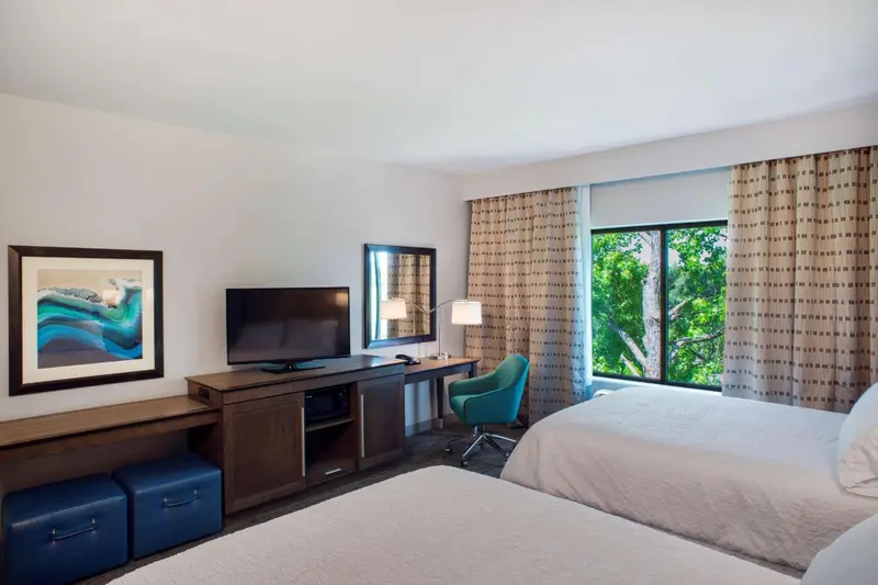 Chambre d'hôtel lumineuse avec deux lits et un bureau près de la fenêtre.