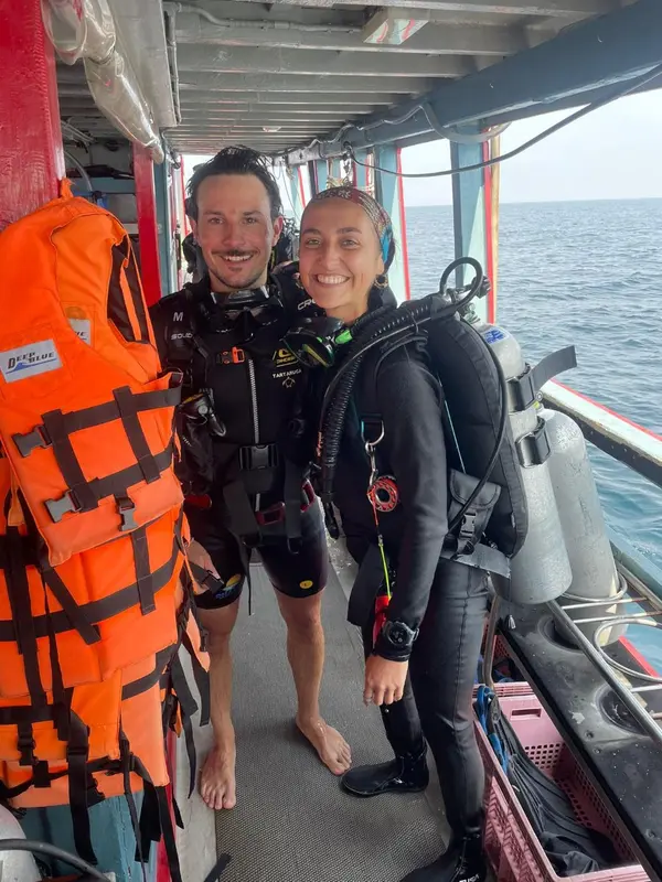 Deux personnes souriantes en combinaison de plongée se tiennent sur un bateau.