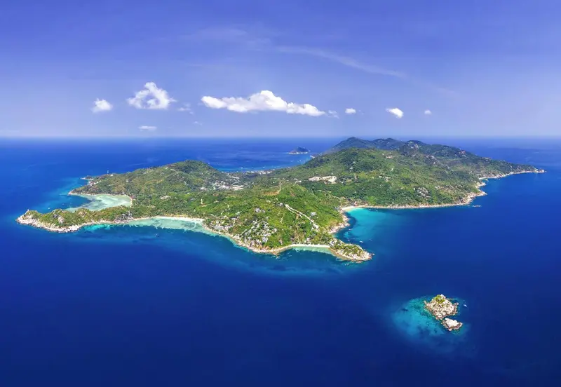 Vue aérienne d'une île tropicale bordée de plages et de végétation luxuriante.