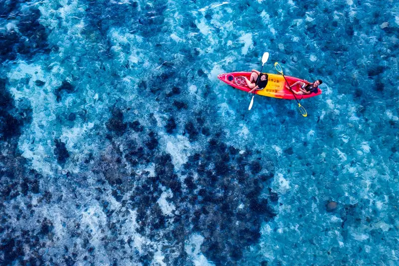Vue aérienne d'un kayak rouge sur une eau turquoise et un récif corallien.
