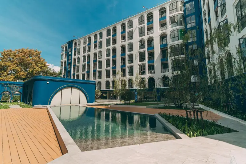 Bâtiment blanc et bleu avec une piscine au premier plan et une végétation luxuriante.