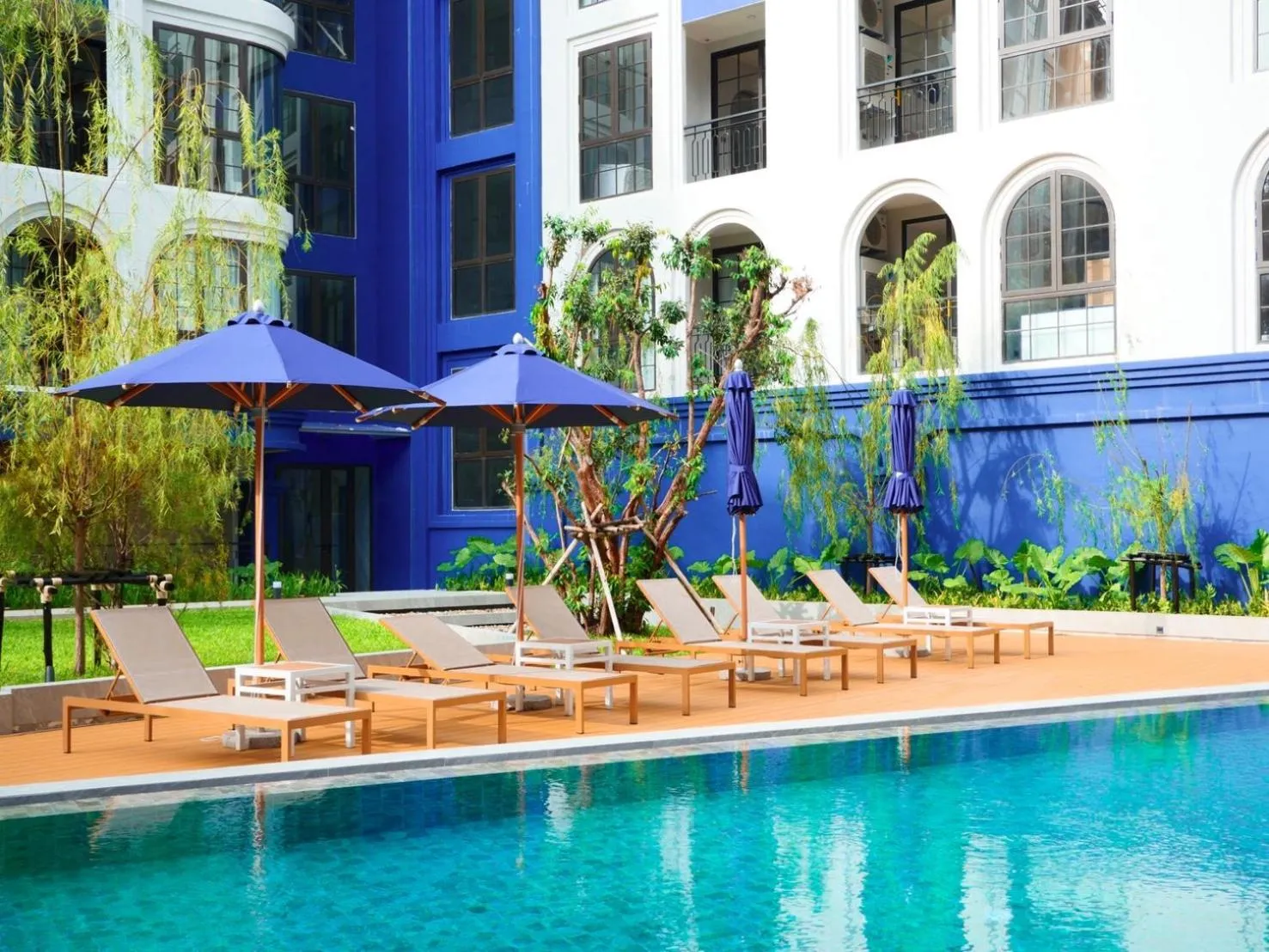 Transats et parasols disposés au bord d'une piscine turquoise dans un jardin tropical.