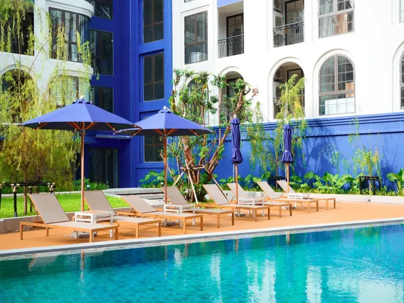 Transats et parasols disposés au bord d'une piscine turquoise dans un jardin tropical.