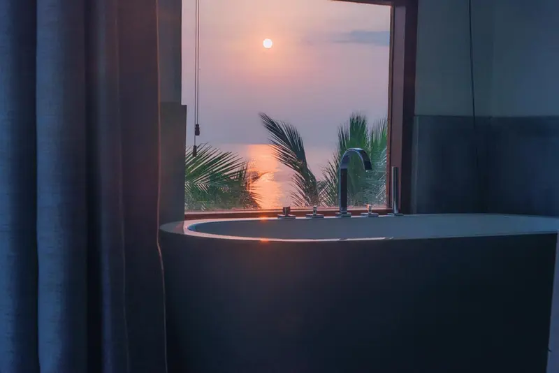 Une baignoire moderne offre une vue sur un coucher de soleil tropical.