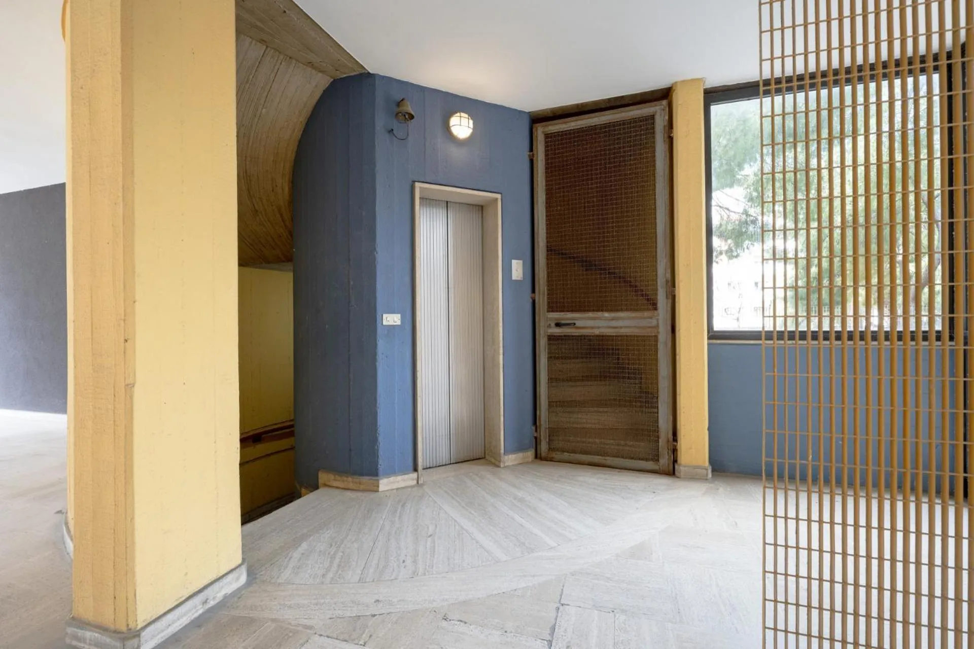 Un ascenseur gris métallique se trouve dans un espace architectural aux murs colorés.