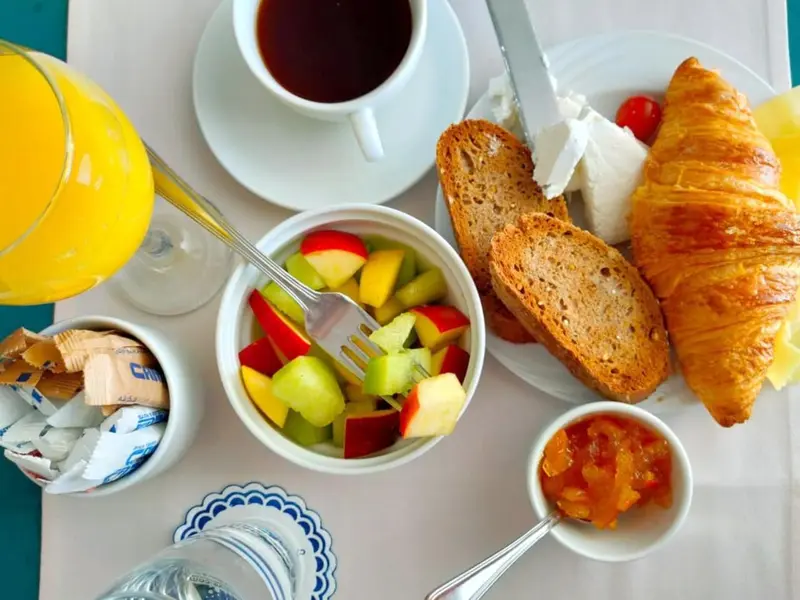 Un petit-déjeuner avec jus d'orange, café, fruits frais et viennoiseries est présenté sur une table.