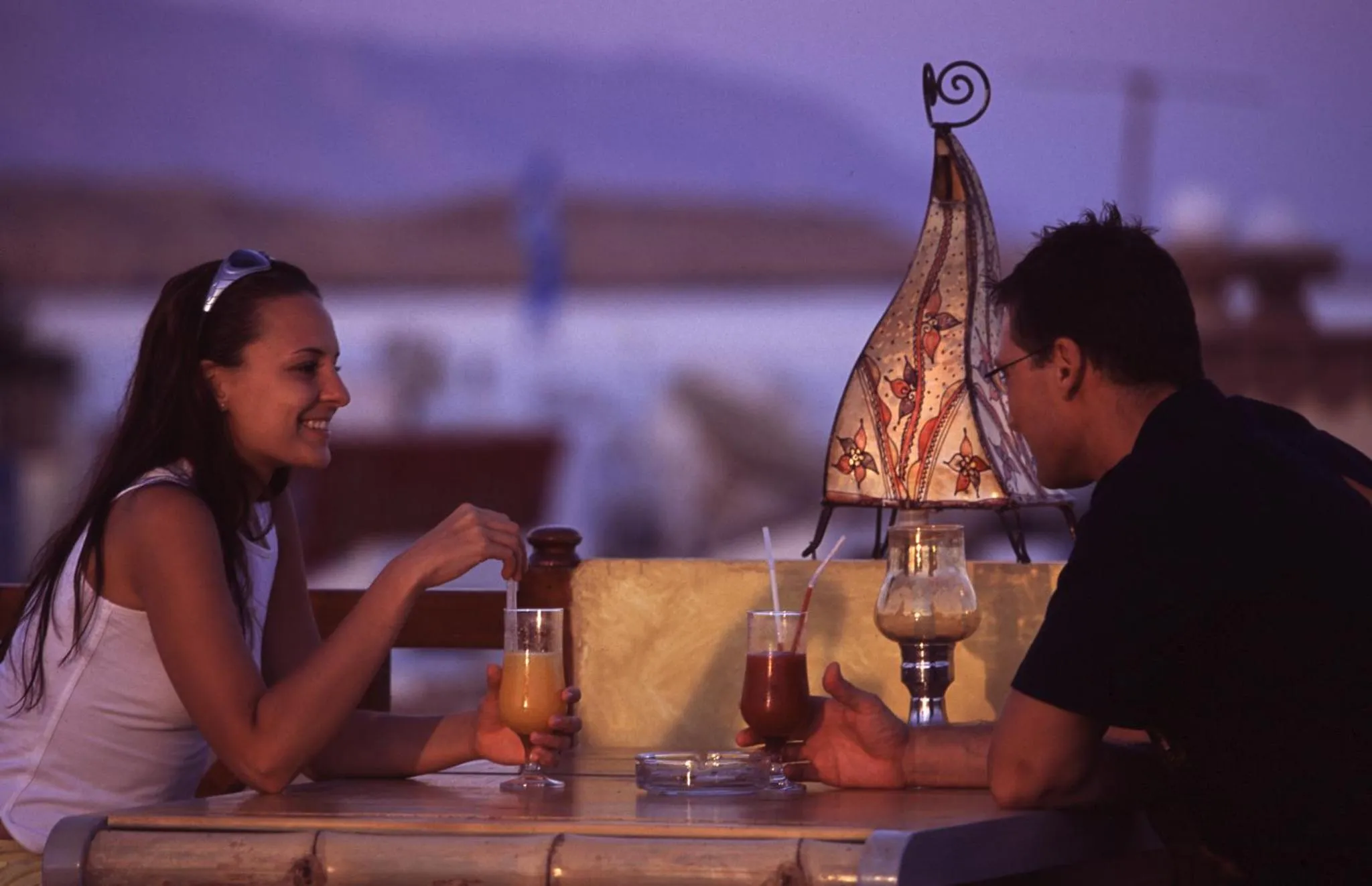 Un couple est assis à une table en extérieur, profitant de boissons au coucher du soleil.