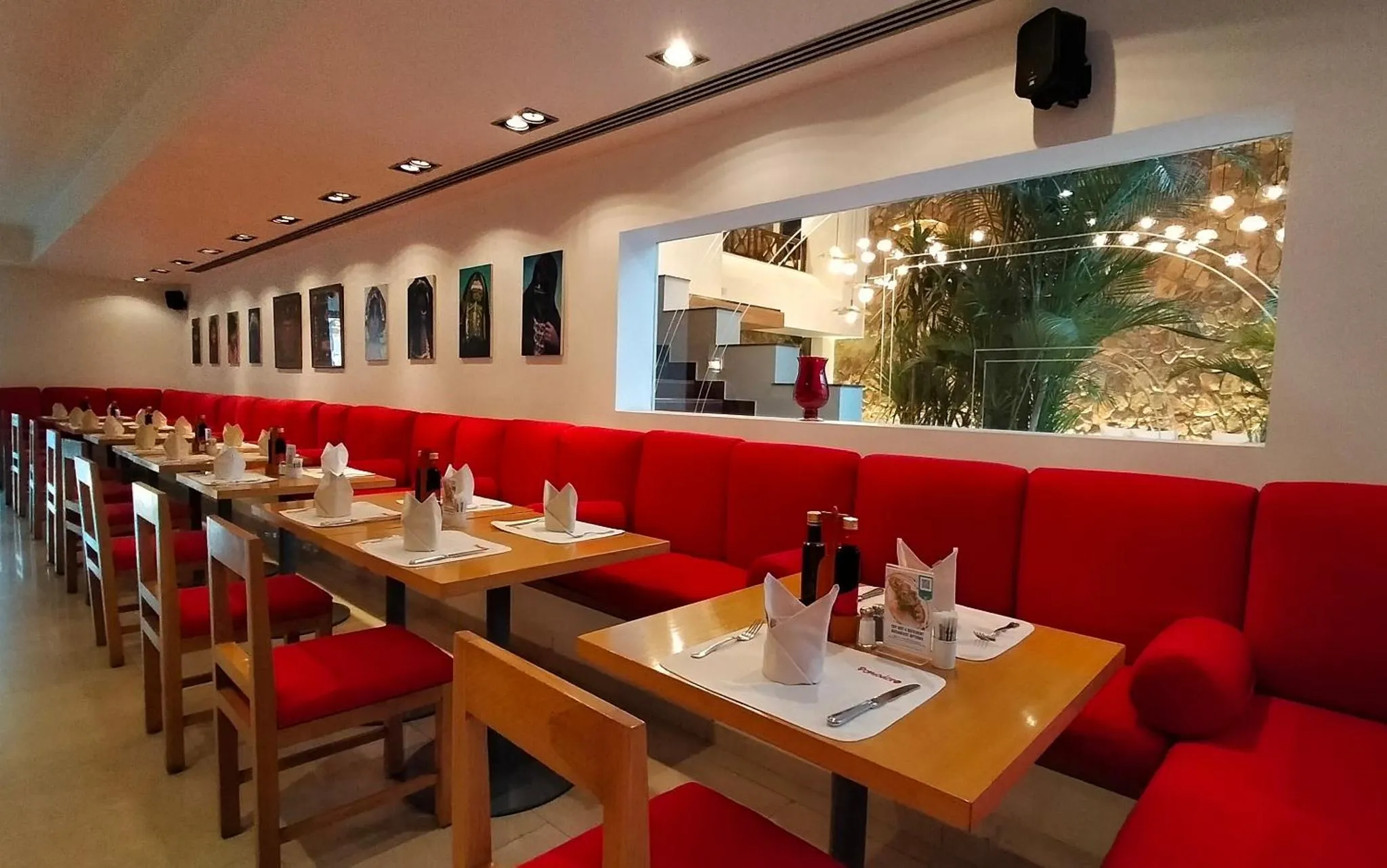 Une salle de restaurant lumineuse avec des tables dressées et des banquettes rouges.
