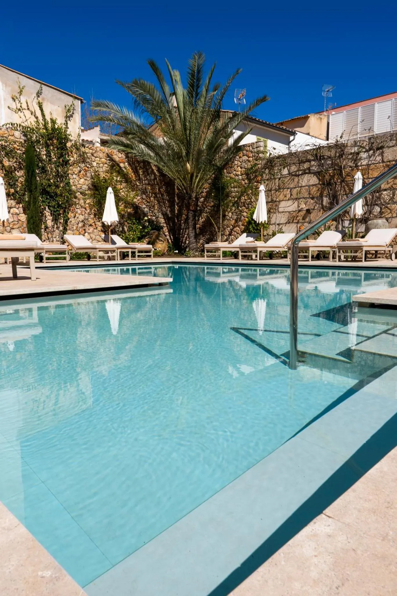 Une piscine rectangulaire avec des transats blancs et des parasols.