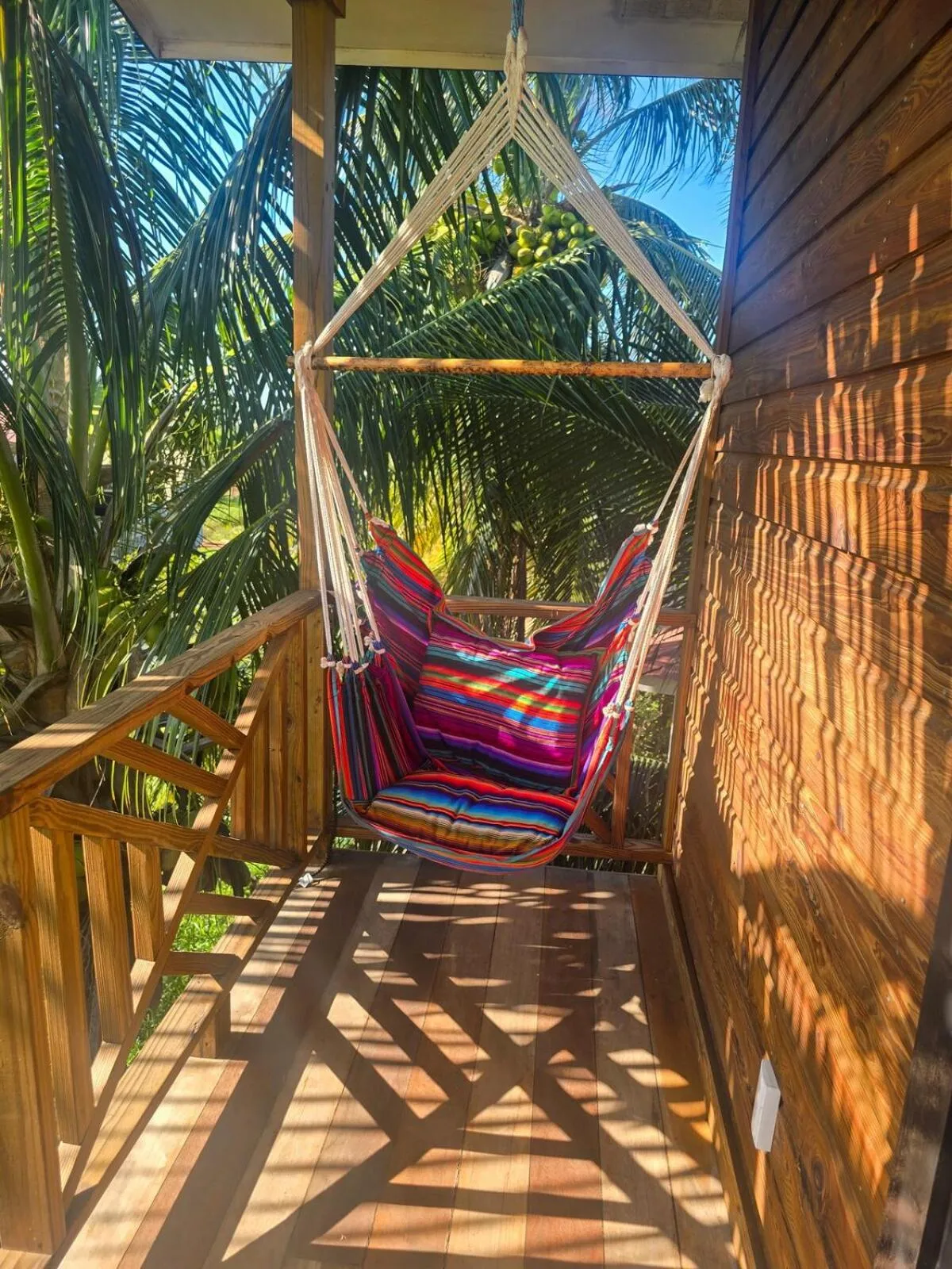 Un hamac coloré est suspendu sur une terrasse en bois ombragée.