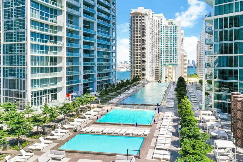 Vue aérienne d'une piscine rectangulaire bordée de transats entre deux immeubles.
