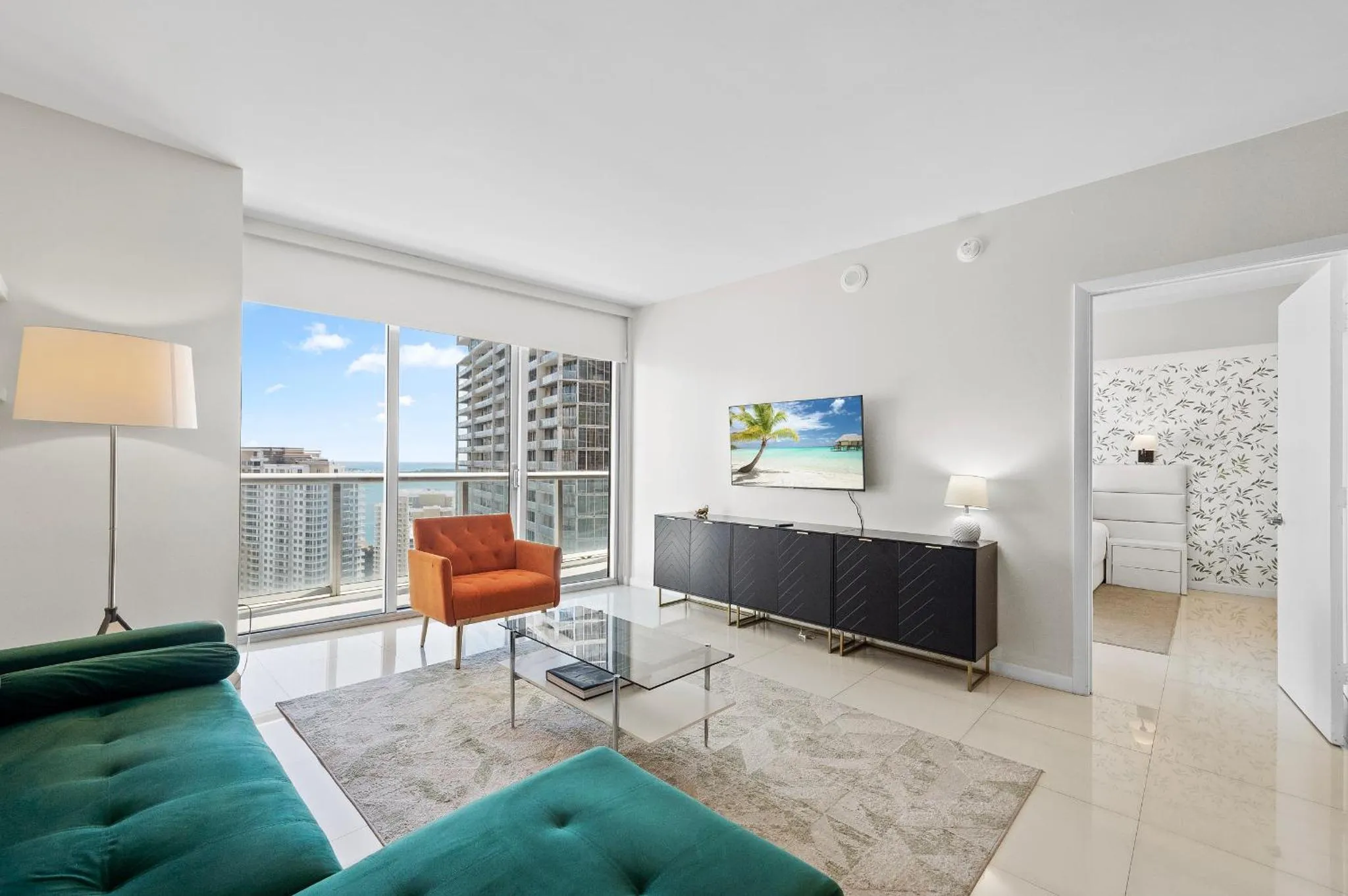 Un salon moderne avec canapé vert, fauteuil orange et vue sur la mer.