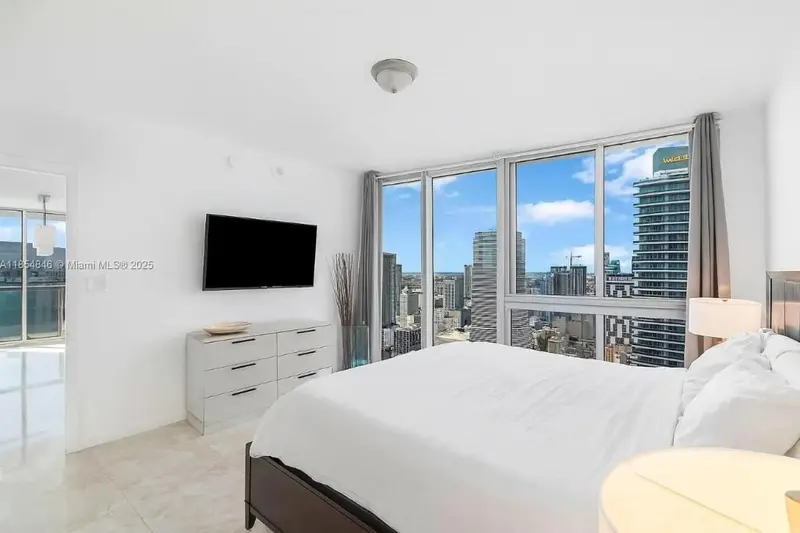 Chambre lumineuse avec un grand lit et une vue sur la ville.