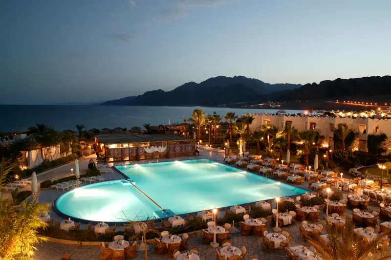 Une piscine illuminée au crépuscule, entourée de tables et de chaises.