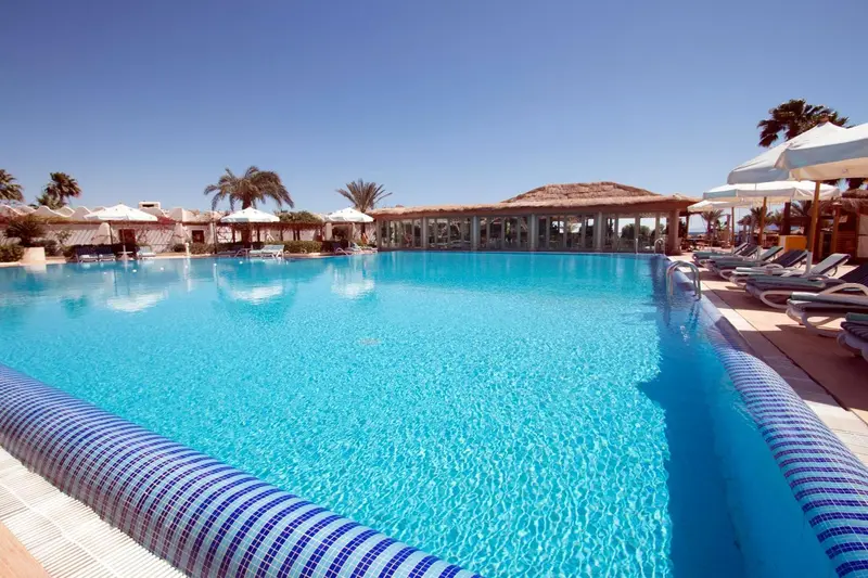 Une piscine turquoise bordée de transats sous des parasols blancs.