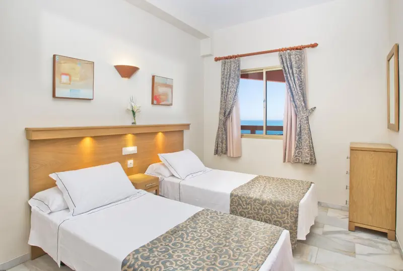 Une chambre lumineuse avec deux lits simples et une vue sur la mer.